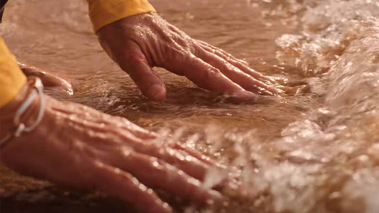 Hands on a beach reaching out to touch a small wave