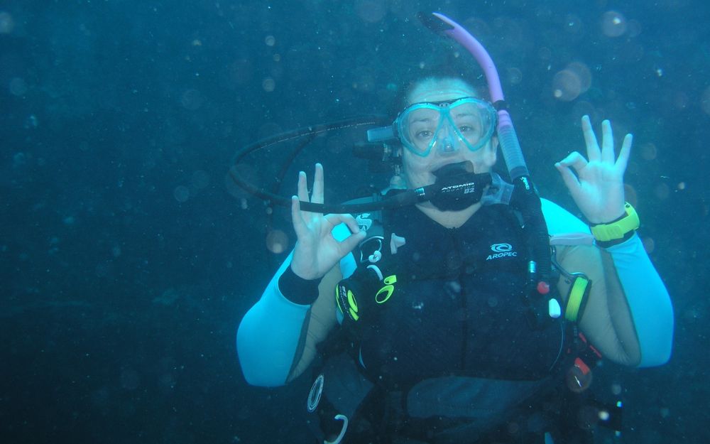 Diver underwater in a blue suit hand-signing okay