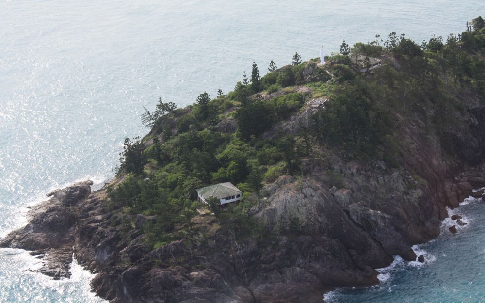 An island with pine trees hosts one small cottage and a helipad. 