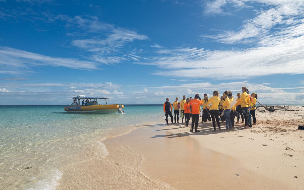 Group of people on a beach with a yellow tender boat in the water.