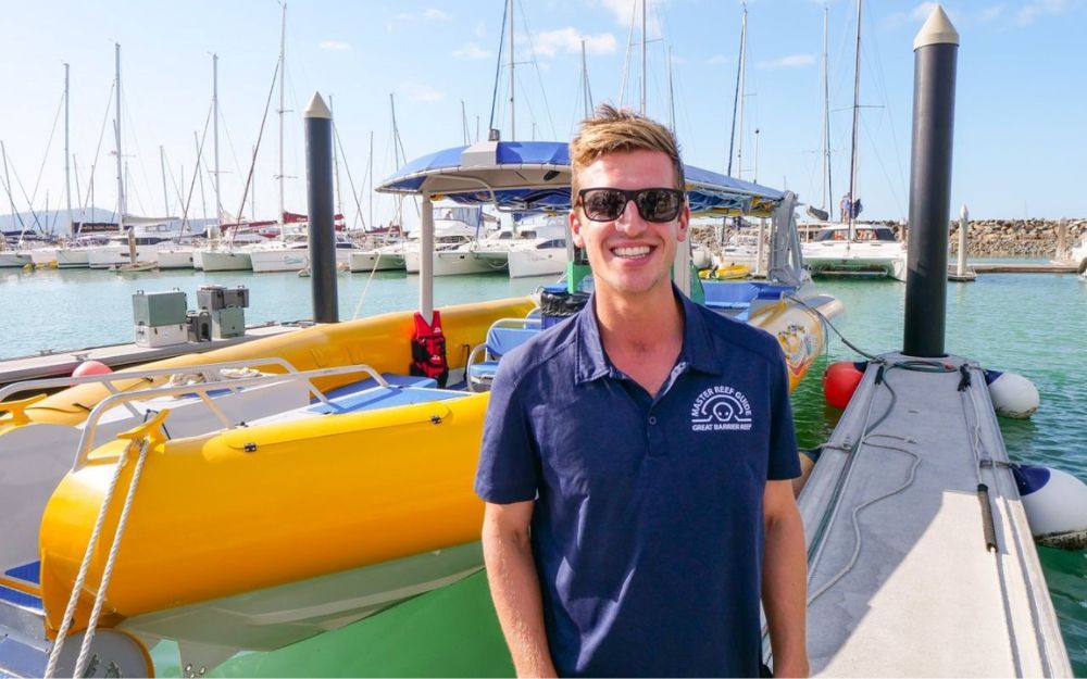 A man in a navy shirt stands in front of a yellow tender boat.