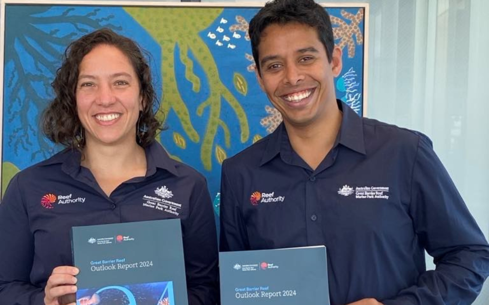 A woman and man in professional attire carry publications called the Outlook Report
