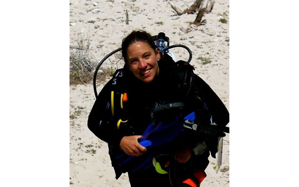 A woman diver poses for a photo on land with her dive gear on