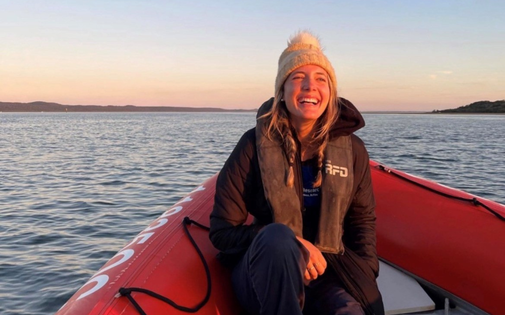 A woman at the helm of a research vessel at sunrise