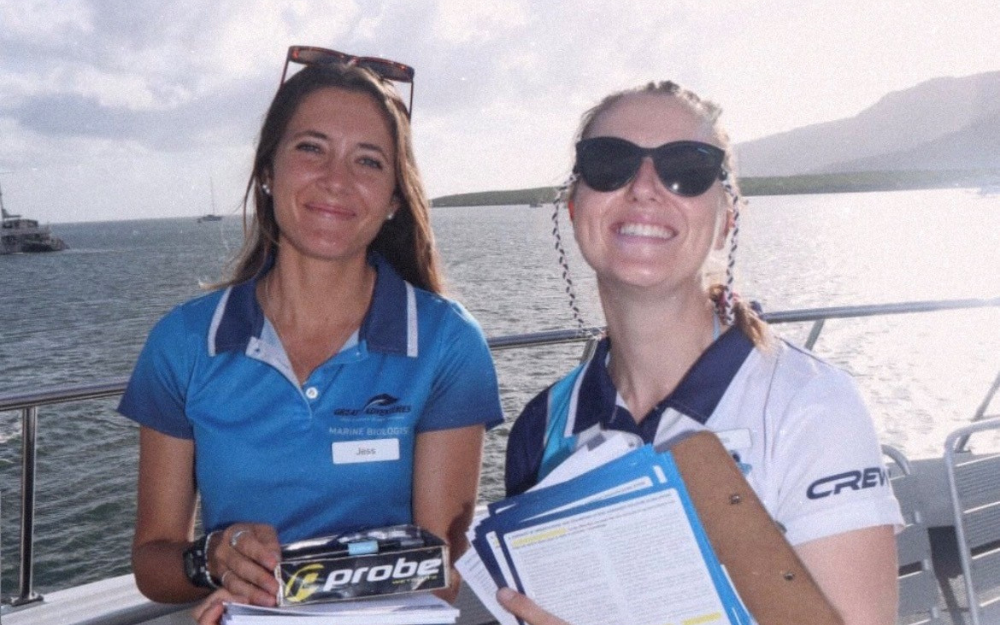 Two boat tour guides holding a clipboard smile for a photo.