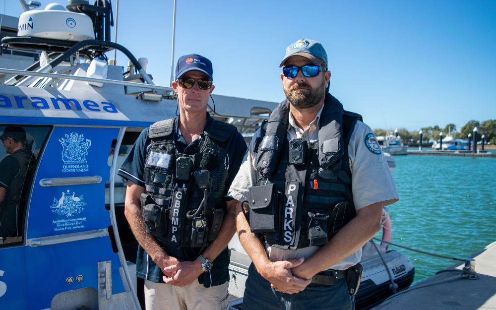 Two compliance officers stand in front of a compliance vessel