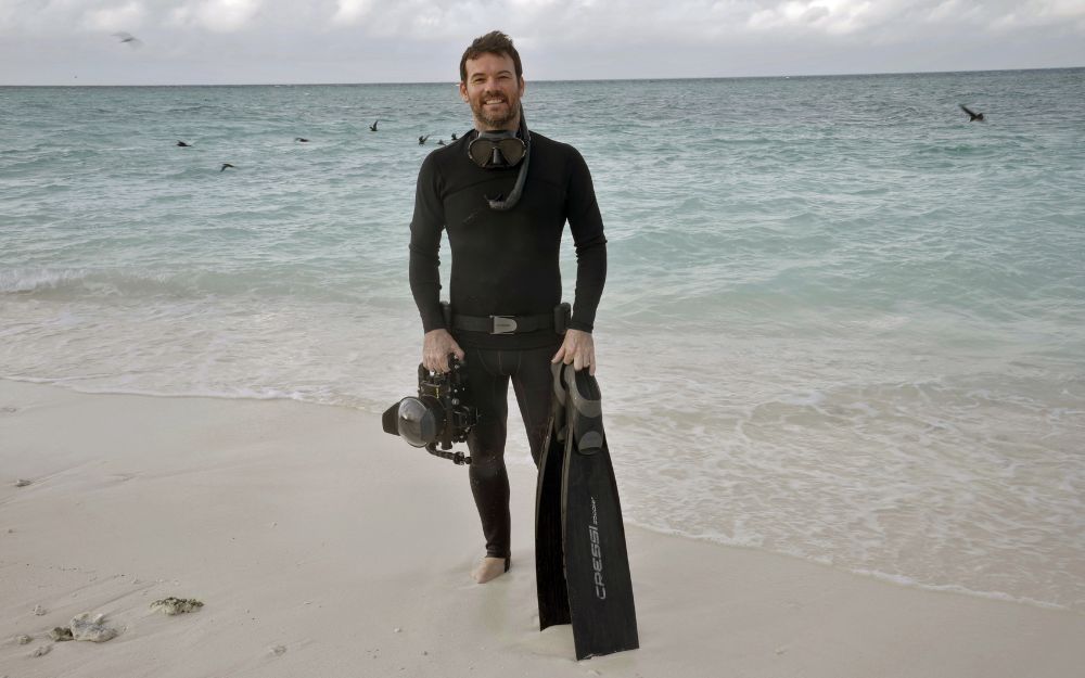 Man standing with camera and snorkelling gear.