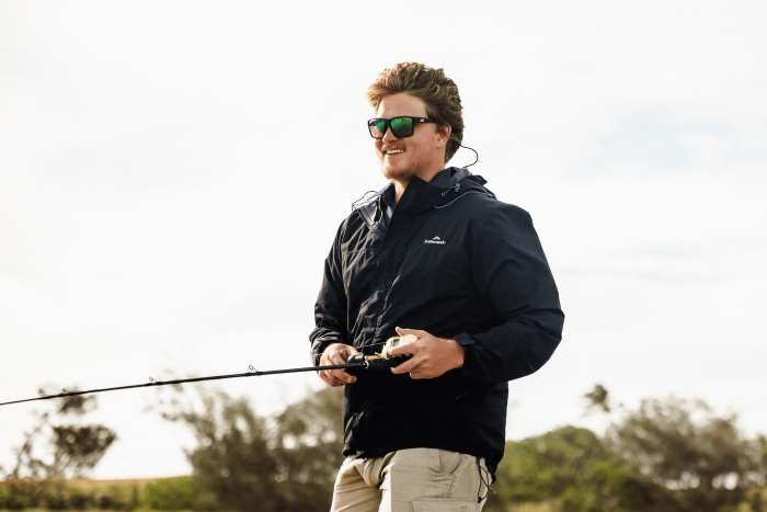 Man standing on a beach, holding a fishing rod and smiling