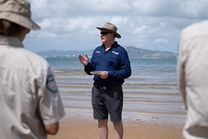 Man speaking on beach with sea and hill in background