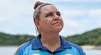 Woman stands on beach looking out into the distance in blue collared shirt. 