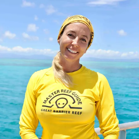 Michelle standing on deck of boat in yellow rashie with reef in background