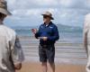 Man speaking on beach with sea and hill in background