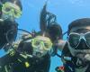 Three scuba divers take a selfie underwater with blue background.