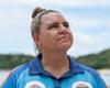 Woman stands on beach looking out into the distance in blue collared shirt. 