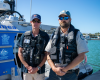 Two compliance officers stand in front of a compliance vessel