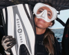 A woman in a snorkel mask holds her fins and smiles for the camera