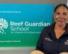 Marica Townsend stands in front of a Reef Guardian School sign in a corporate button up shirt.