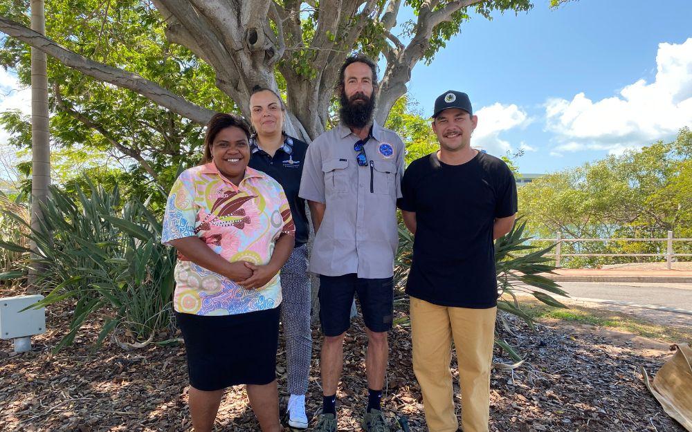 Four people standing in front of tree