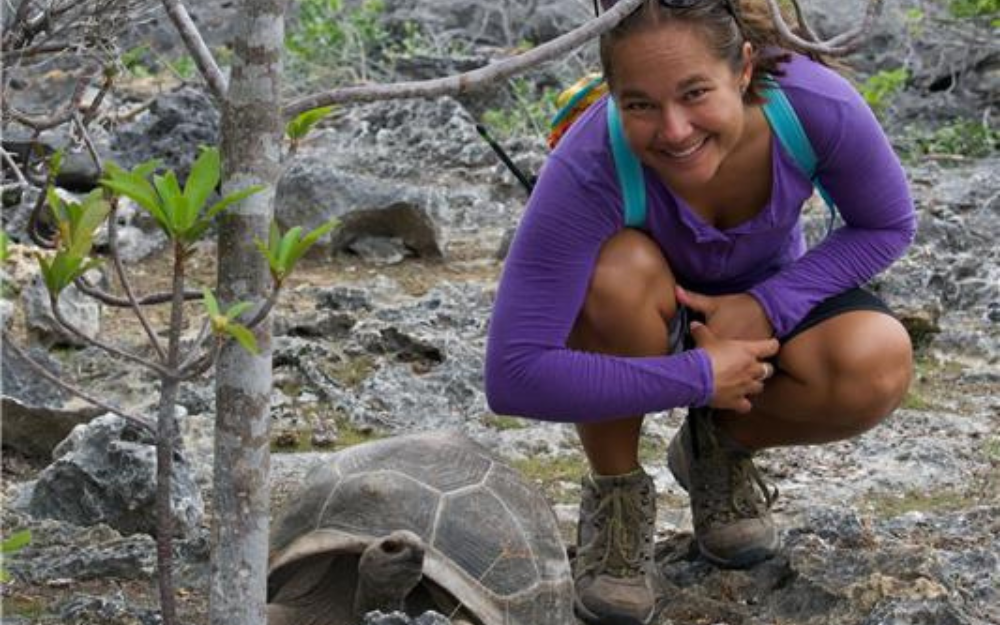 Woman in purple shot poses for a photo with giant tortoise.