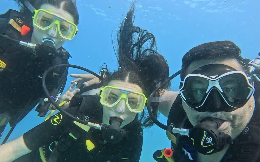 Three scuba divers take a selfie underwater with blue background.