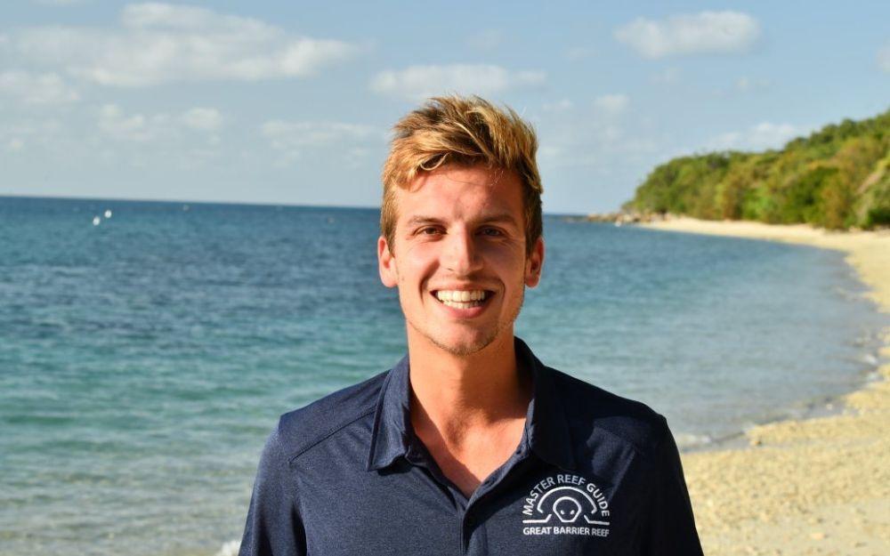 A man stands on a beach with thick vegetation in the background.
