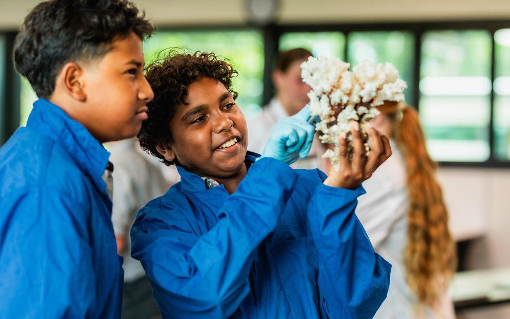 Two students in blue lab coats inspect a dried coral skeleton