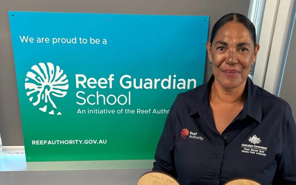 Marica Townsend stands in front of a Reef Guardian School sign in a corporate button up shirt.